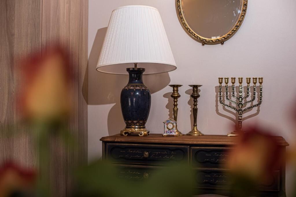 A lamp, a menorah, a clock, and a mirror on a wooden dresser.