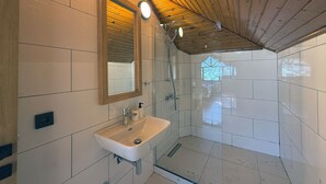 Un baño moderno con techo de madera, un espejo grande, un lavabo y una zona de ducha.