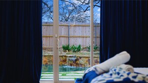 A room with a large sliding glass door leading to a backyard with a wooden fence, a small waterfall feature, and a pool. - 1110 Terjo Ln (Austin)
