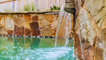 Eine Steinsäule mit Wasserspiel, Pool und Holzlattenzaun.