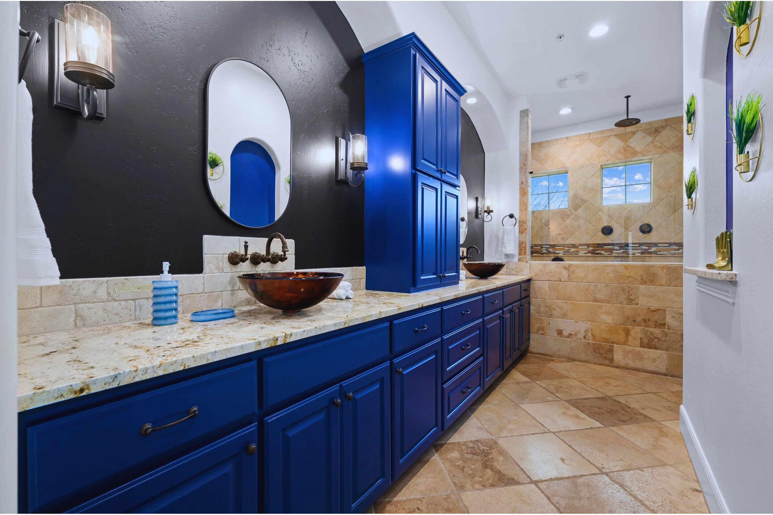 A modern kitchen with blue cabinets, a large oval mirror, and a stone backsplash.