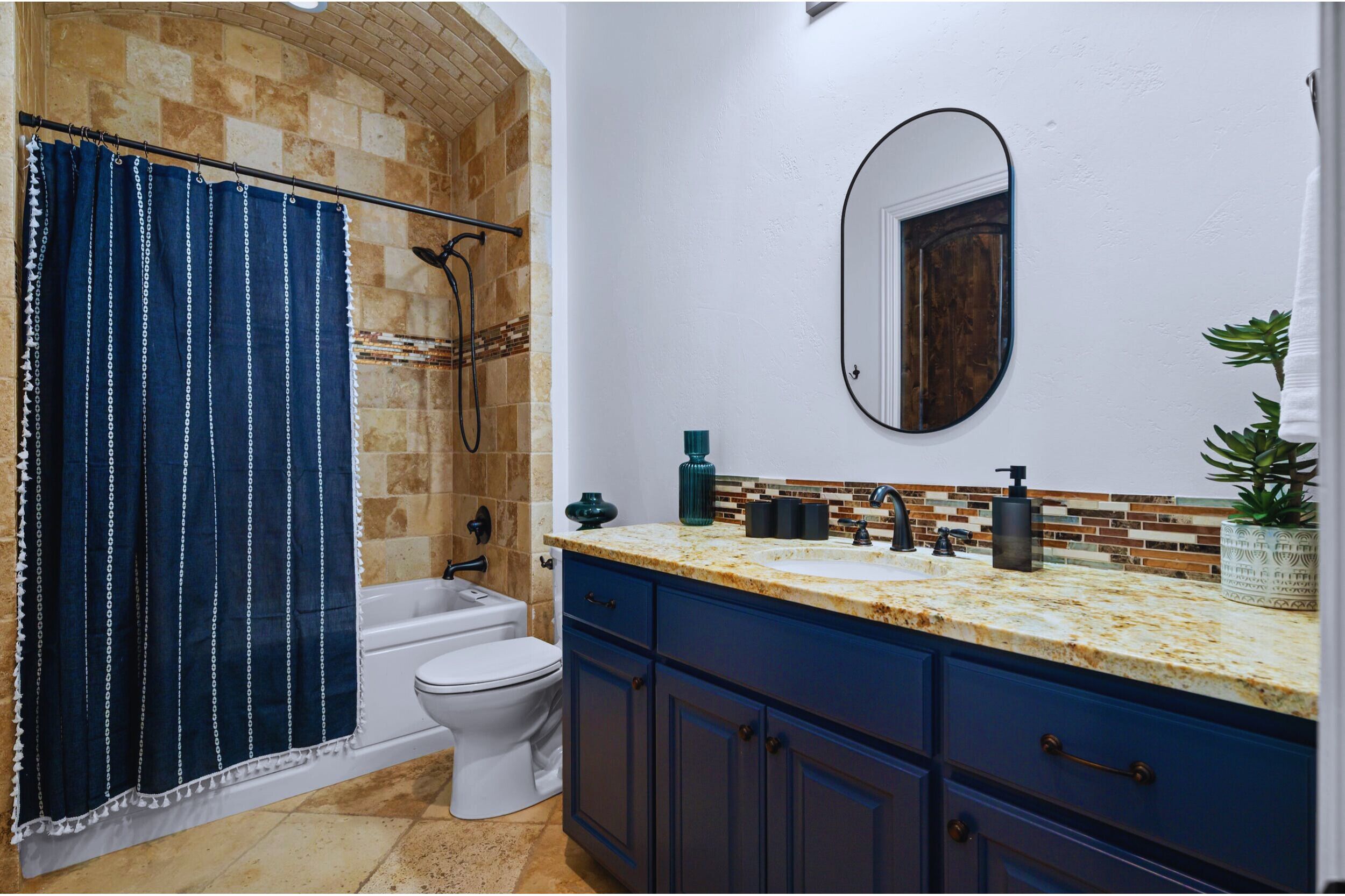 Un baño con cortina de ducha, inodoro, lavamanos con espejo y una planta en maceta.