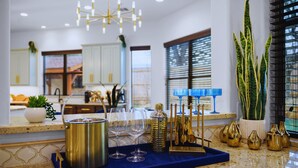 A kitchen with a blue countertop, stainless steel cookware, wine glasses, and a gold utensil holder. - 1110 Terjo Ln (Austin)