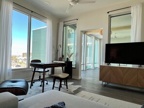 Ein modernes Wohnzimmer mit einem großen Fernseher, einem Schreibtisch und einer gemütlichen Sitzecke.