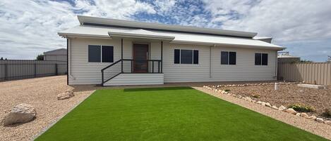 A modern two-story house with a well-maintained lawn, a front porch with a staircase, and a clear sky.