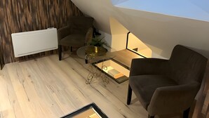 A modern loft bedroom with a sloped ceiling, a skylight, a radiator, a glass coffee table, and two armchairs. - Holiday Home “Gîte Le Pré Salé” with Private Terrace and Wi-Fi (Boismont)