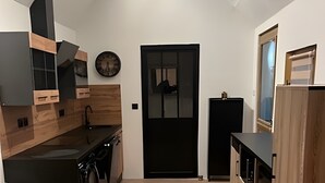 A modern kitchen with wooden cabinetry, a black door, and a dining area with a wooden table. - Holiday Home “Gîte Le Pré Salé” with Private Terrace and Wi-Fi (Boismont)