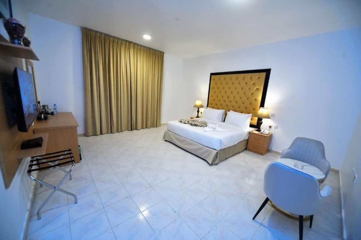 Una habitació d'hotel amb un llit, dues làmpades de nit, un escriptori amb una cadira, una televisió i una finestra amb cortines.