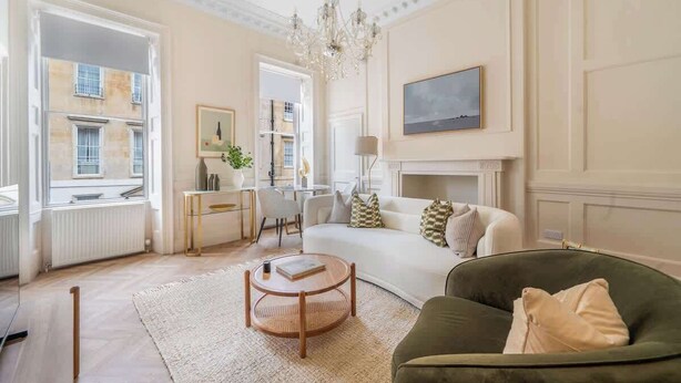 A living room with a sofa, a green armchair, a coffee table, a chandelier, and a fireplace. - Modern Comfort in a Classic Bath Setting - VAT Q (Bath)