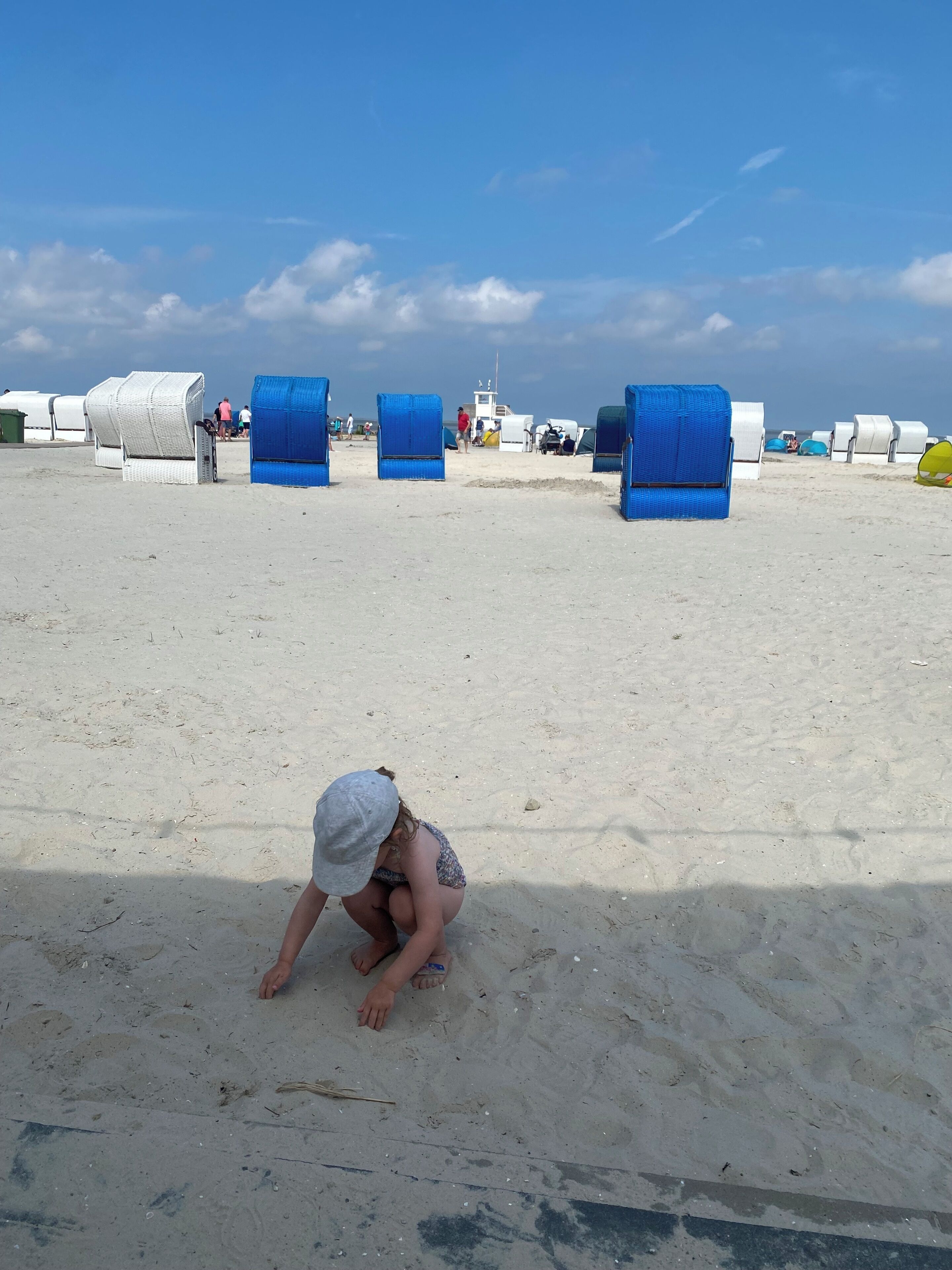 A sandy beach with blue and white beach chairs, a boat in the background, and a person in the foreground.