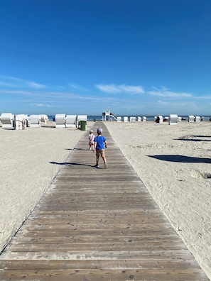 A wooden boardwalk leading to beach huts with a lifeguard tower in the distance.