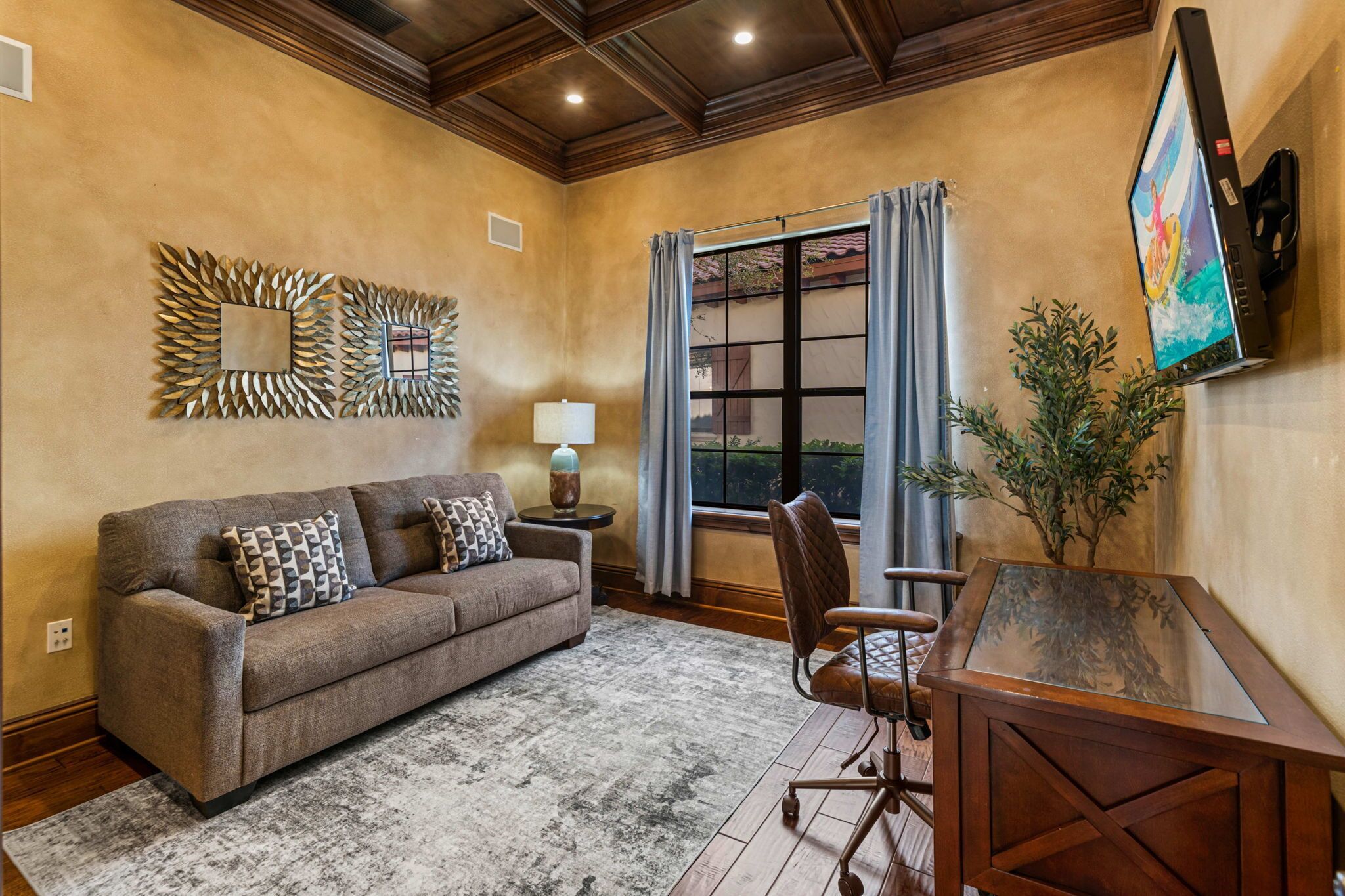 A living room with a sofa, a chair, a table, a lamp, a decorative mirror, and a TV mounted on the wall.
