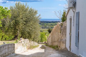 Un sentiero stretto che conduce a un edificio con un muro in pietra e vista sul paesaggio costiero.