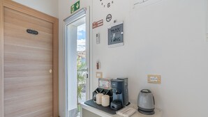 Habitación de hotel con una puerta de madera que indica 'TOILETTE', una cafetera, dos tazas y un hervidor sobre una pequeña mesa.