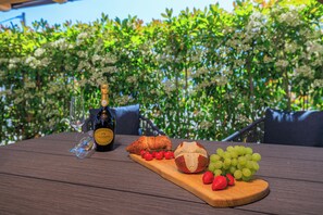 Ein Holztisch mit einer Weinflasche, einem Glas, einem Croissant, Cocktailtomaten, Trauben und Erdbeeren.
