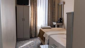 Una habitación de hotel con cama, escritorio, televisor, armario, espejo y aire acondicionado.