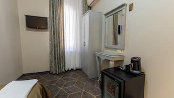 Una habitación de hotel con una cama, un escritorio pequeño, un refrigerador, un televisor y un espejo.
