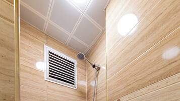Een douche met beige tegels, ventilatie en een handdouche.