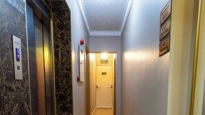 Un couloir aux murs de marbre, un ascenseur et une porte indiquant « 4e étage ».