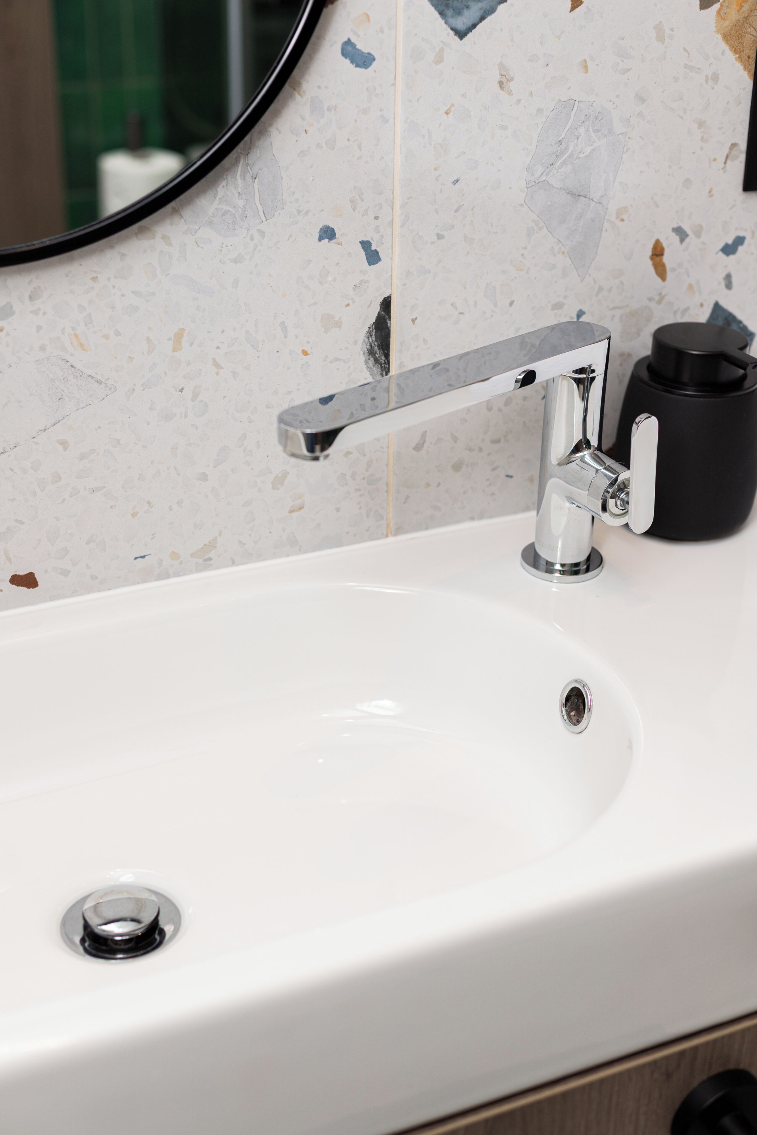 A bathroom sink with a chrome faucet, a black cup holder, and a mirror.