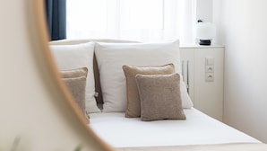 A bed with white bedding and multiple pillows, a bedside table with a lamp, and a window with curtains. - Native Apartments Karłowicza 13 (Kraków)