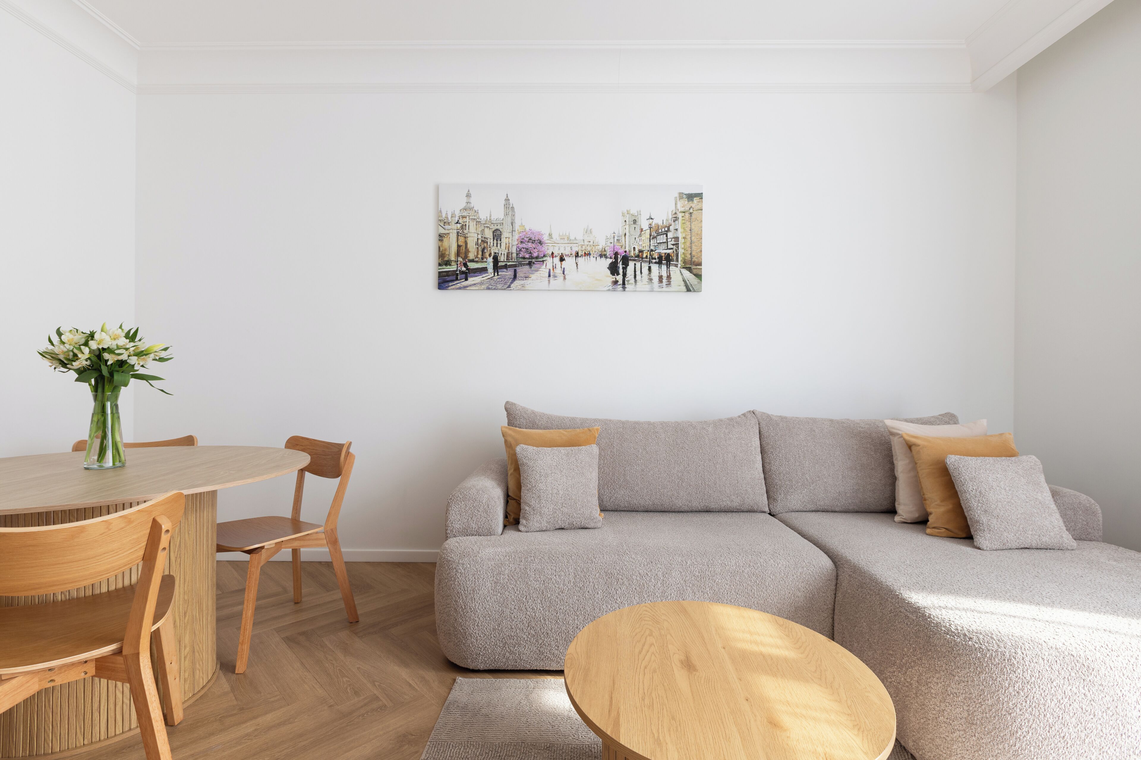A living room with a sofa, a round wooden coffee table, a dining table with chairs, and a vase with flowers.