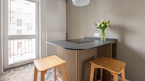 A modern kitchen with a central island, two wooden stools, a vase with flowers, and a window with blinds. - Native Apartments Karłowicza 13 (Kraków)