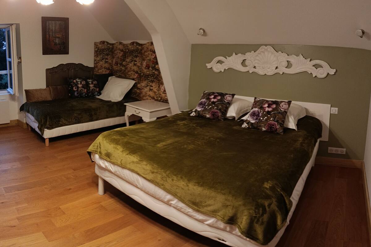 A bedroom with two beds, a wooden floor, a chandelier, a painting, and a floral-patterned headboard.