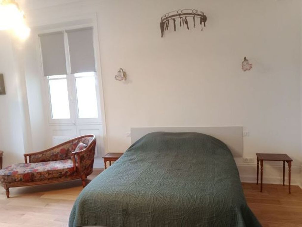 A bedroom with a bed, a chair, a small table, and a wall-mounted light fixture.