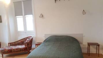 A bedroom with a bed, a chair, a small table, and a wall-mounted light fixture.
