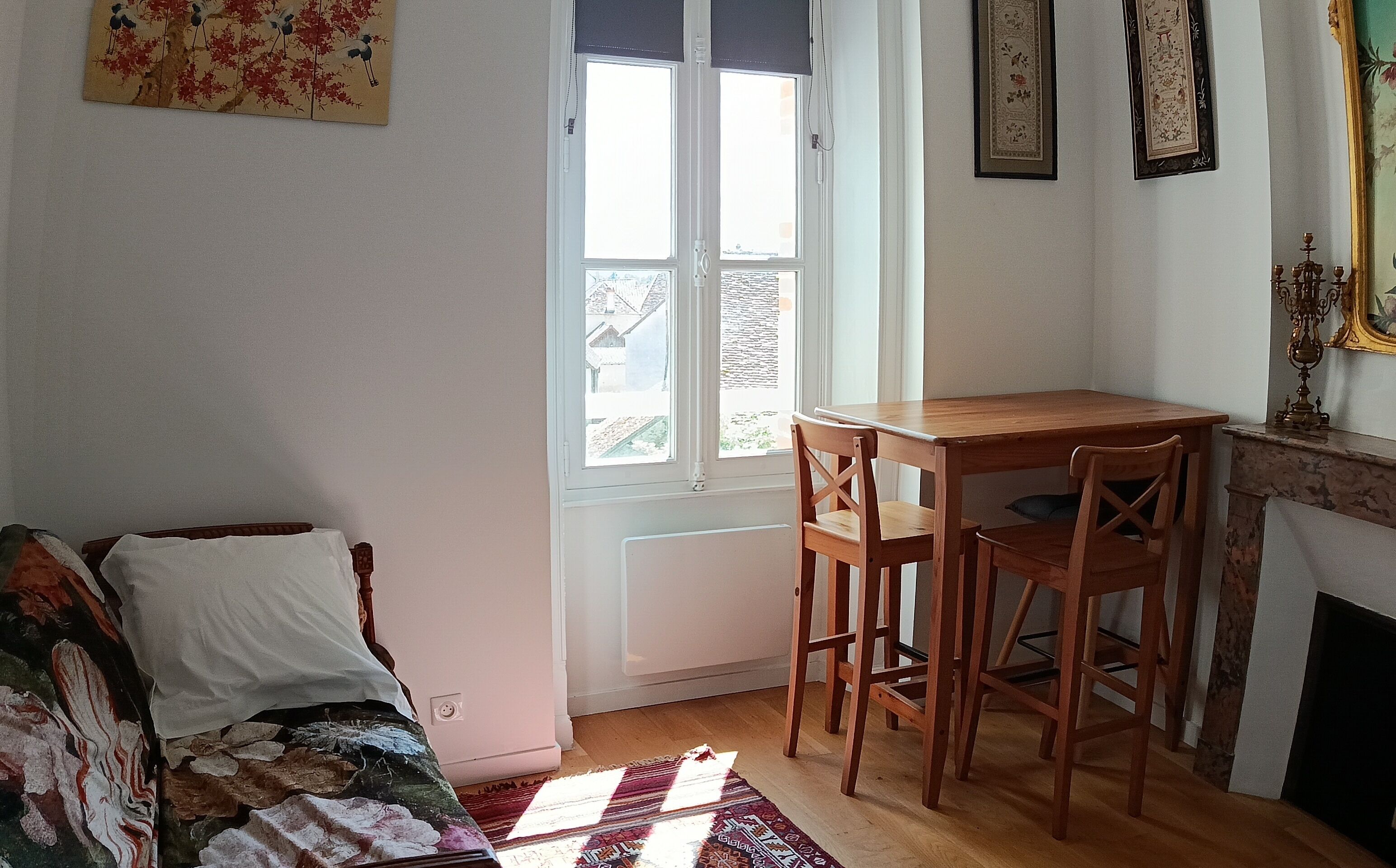 Una habitación con una mesa de madera, dos sillas, un sofá, una ventana con persianas y una chimenea.