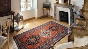 A room with exposed wooden beams, a fireplace, a large mirror, and a patterned rug. - VILLA SAINT-PIERRE (La Trimouille)