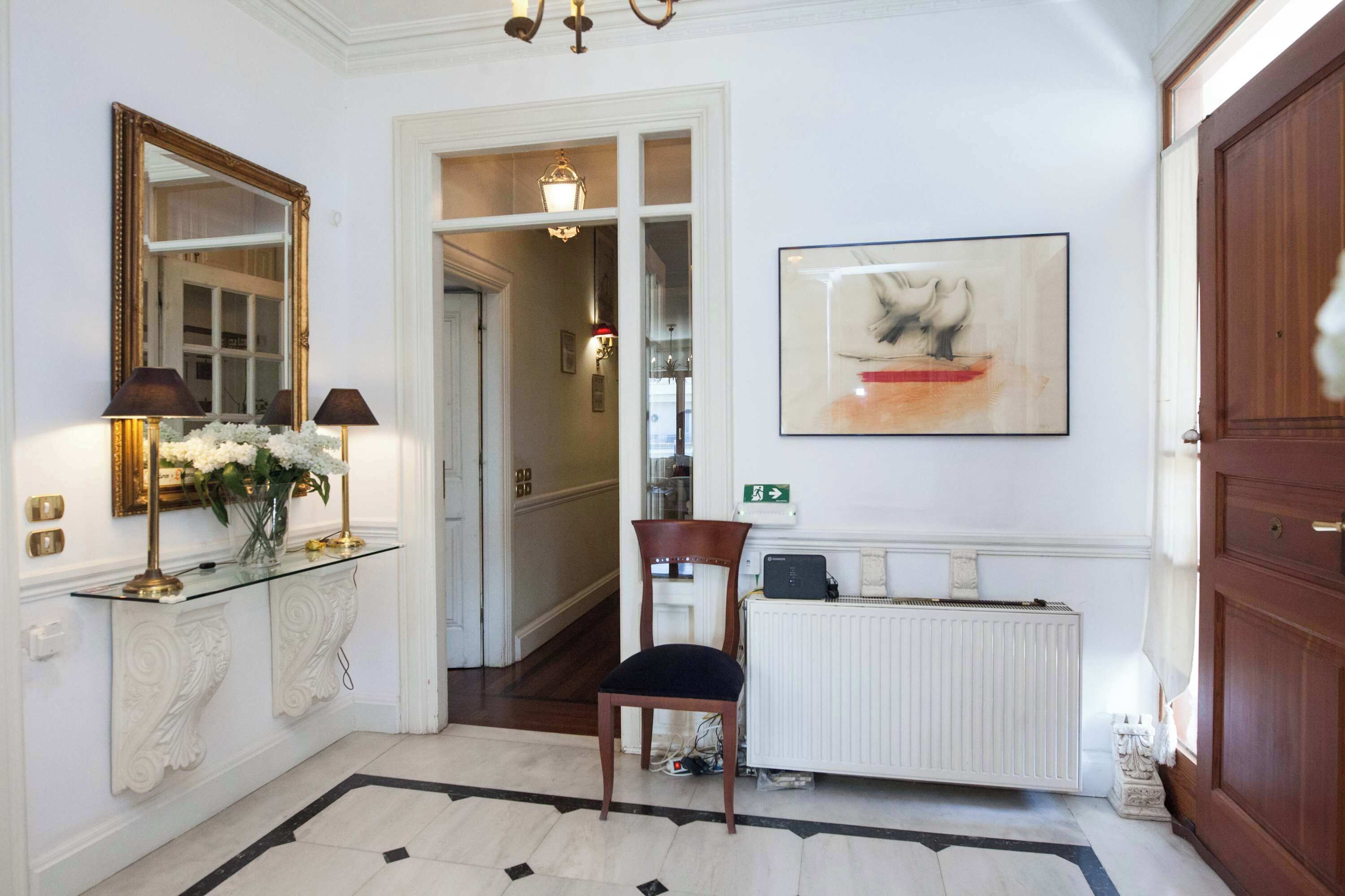 A hallway with a mirror, a chair, a radiator, and a framed artwork on the wall.