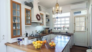 Una cocina con armarios de madera, una isla central con cuencos de fruta, una lámpara de araña y vistas al exterior a través de una ventana.