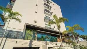 A modern building with a glass facade, palm trees, and a visible address number. - Apt in Condo w/ Pool 110m From the Beach Vem0306 (João Pessoa)