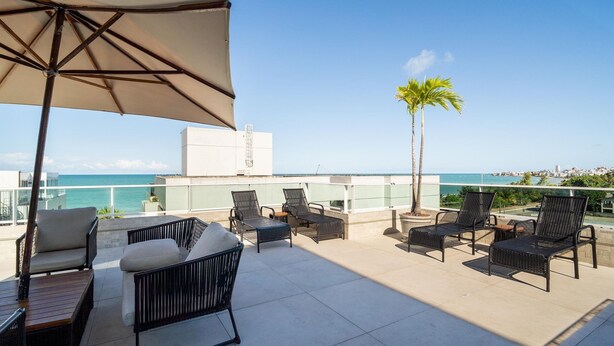A rooftop terrace with outdoor seating, a palm tree, and a view of the ocean. - Apt in Condo w/ Pool 110m From the Beach Vem0306 (João Pessoa)