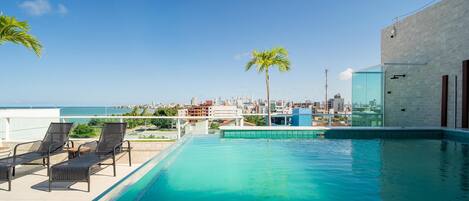 A rooftop pool with lounge chairs and a city view.