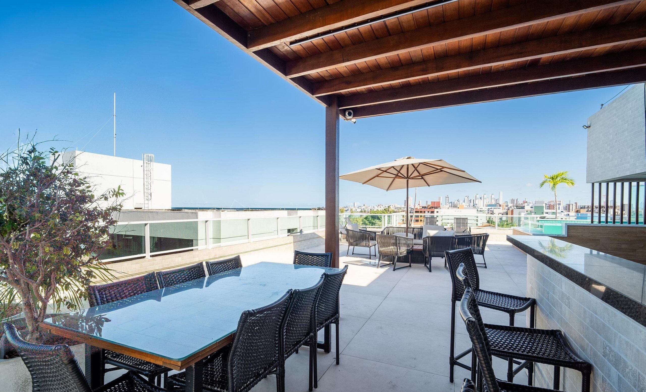 Um terraço no topo com mesa de vidro, cadeiras de vime e um grande guarda-sol.