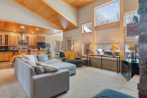 Ein großzügiger Wohnbereich mit einem großen, grauen Ecksofa, einer Küche mit Holzausbau und einem Essbereich mit Tisch und Stühlen.