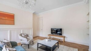 A modern living room with a sofa, armchair, coffee table, TV, and chandelier. - Prime Location! 1-Bed Flat Nr Attractions - VAT Q (Bath)