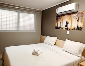 A hotel room with a bed, a window with a grid pattern, an air conditioning unit, and a painting of a couple by a tree. - Manaíra Palace - Michel  (João Pessoa)