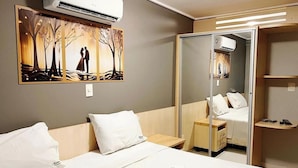Ein Hotelzimmer mit einem Bett, einem Nachttisch, einem Spiegel, einer Klimaanlage und einem Bild an der Wand.