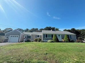 A two-story house with a garage, a front lawn, and a well-maintained garden. - Charming 2-bedroom pet friendly house with central AC in quiet Dennis Port area (Dennis)