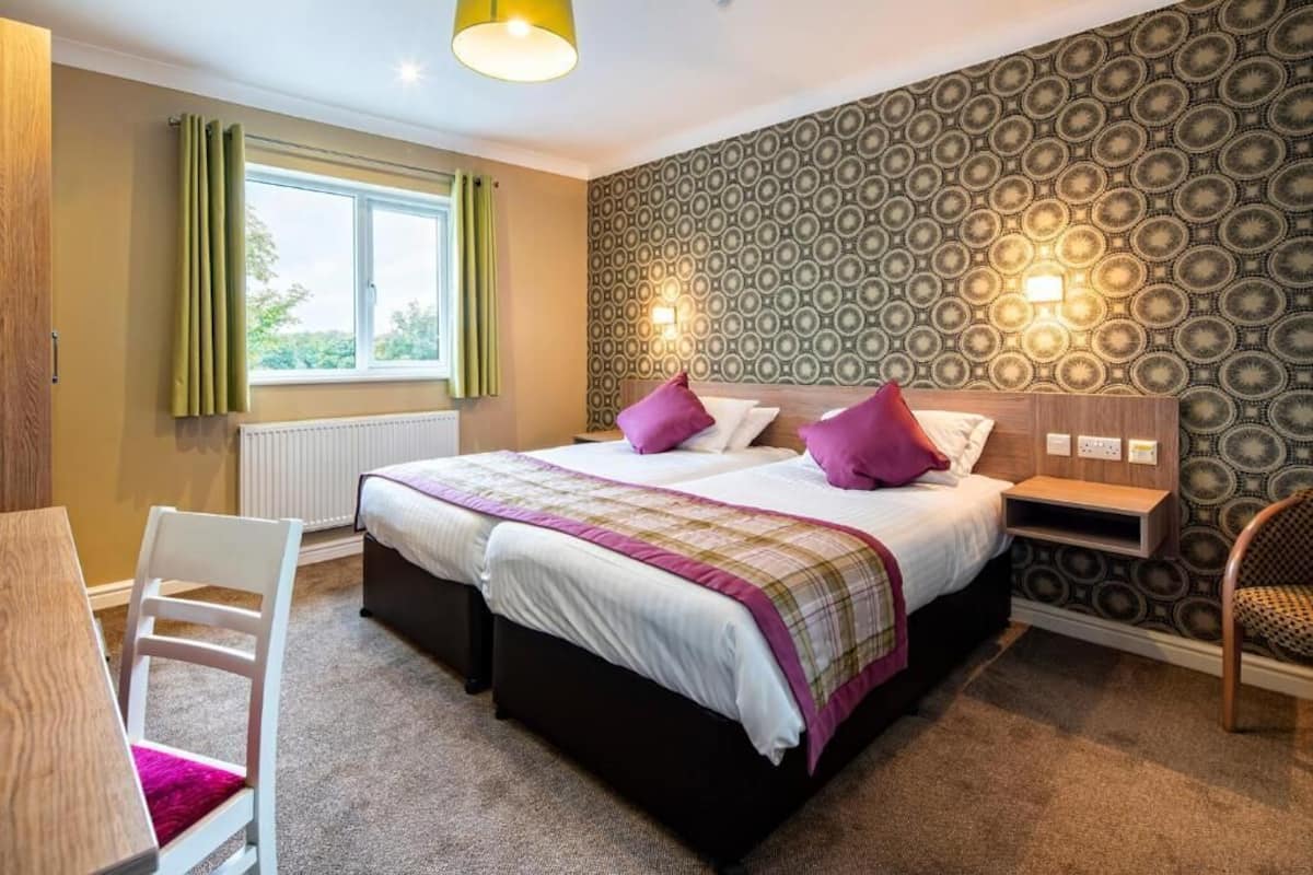 A bedroom with a bed, bedside tables, a chair, a window with curtains, and a patterned wall.