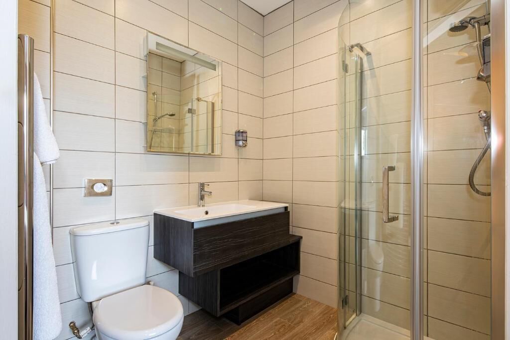 A modern bathroom with a glass shower enclosure, a white toilet, and a dark wood vanity.