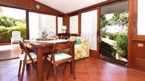 Un comedor con una mesa y sillas de madera, un cojín floral, y vistas a la vegetación a través de un ventanal corredero.