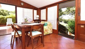 Ein Essbereich mit Holztisch und -stühlen, einem floralen Kissen und Blick auf Grün durch eine Schiebetür.
