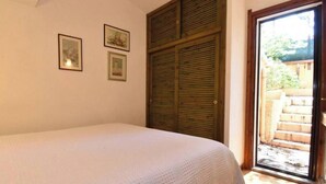 Un dormitorio con cama, una puerta de madera y vista a un jardín a través de una puerta de cristal.