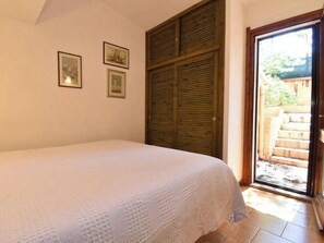 Un dormitorio con cama, una puerta de madera y vista a un jardín a través de una puerta de cristal.