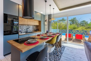 A modern kitchen with a large island, built-in oven, and dining area with chairs and a view of the outdoors. - Modern House with a Pool in Crikvenica (Crikvenica)